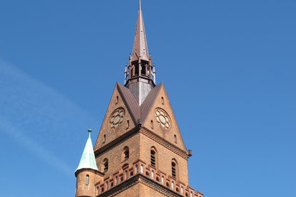 Die Turmspitze der Herz-Jesu-Kirche ragt in den blauen Himmel - Copyright: Ev.-Luth. Kirchenkreis Lübeck-Lauenburg